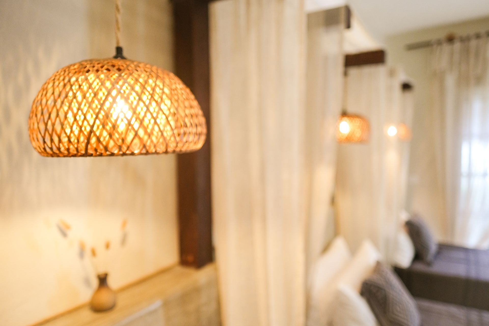 Woven pendant lamp illuminates a spa-like setting with draped curtains and cushioned seating.