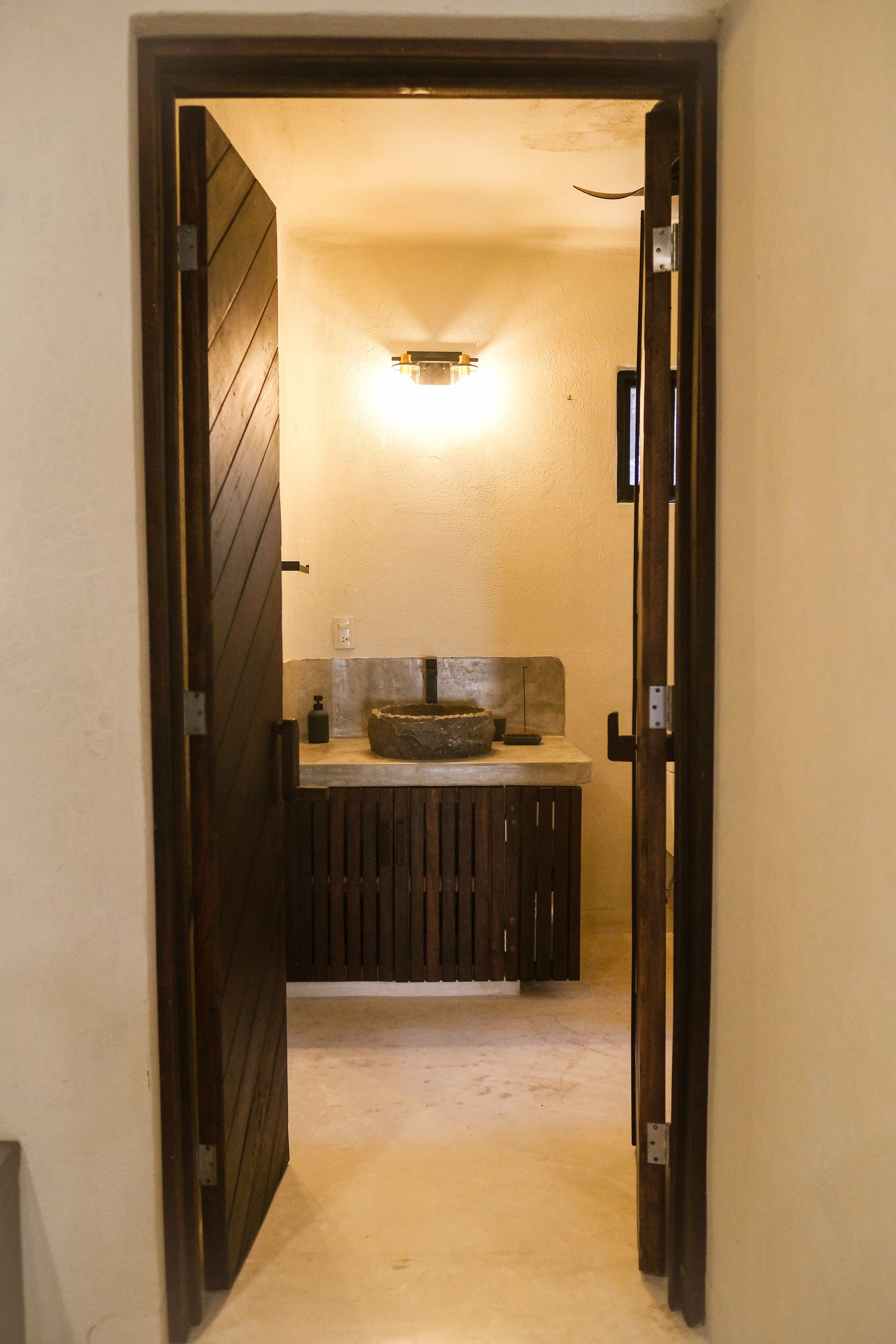 Open wooden door leads into a bathroom with a sink, light fixture, and textured wall.