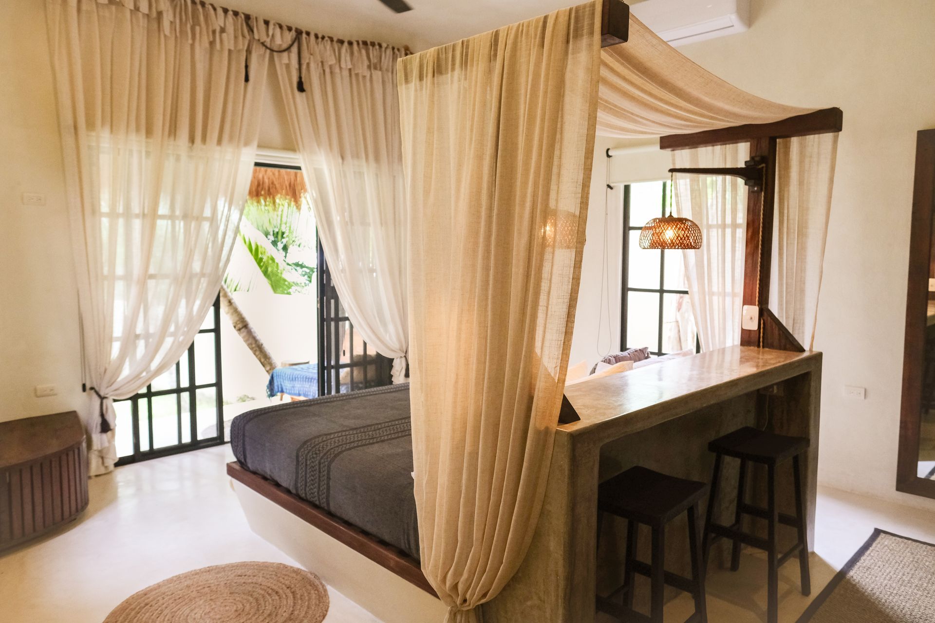 Bedroom with canopy bed, bar, and outdoor view through windows, decorated in beige and light wood tones.
