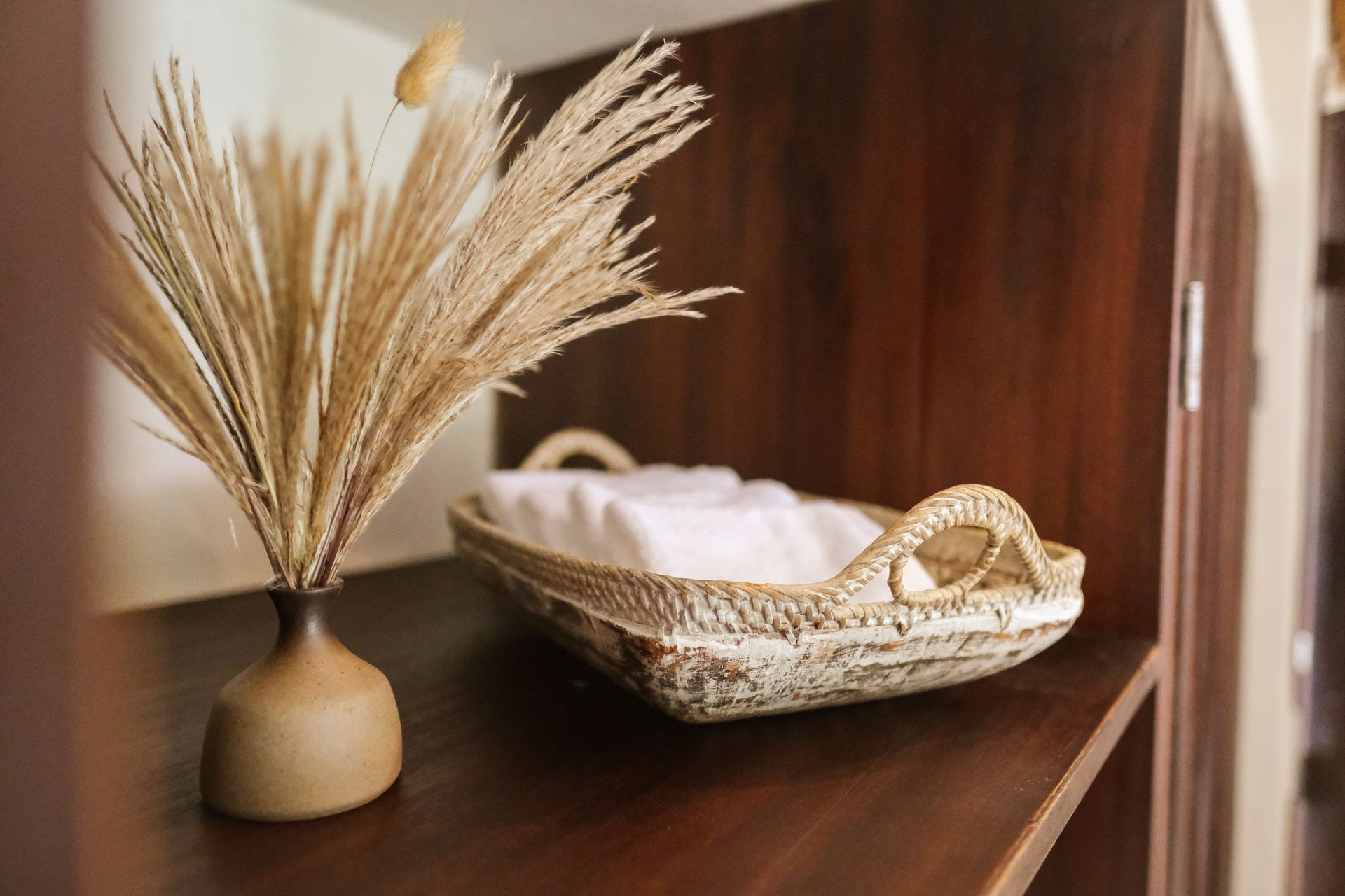 Shelf with vase of dried grass and wicker basket holding folded white towels.