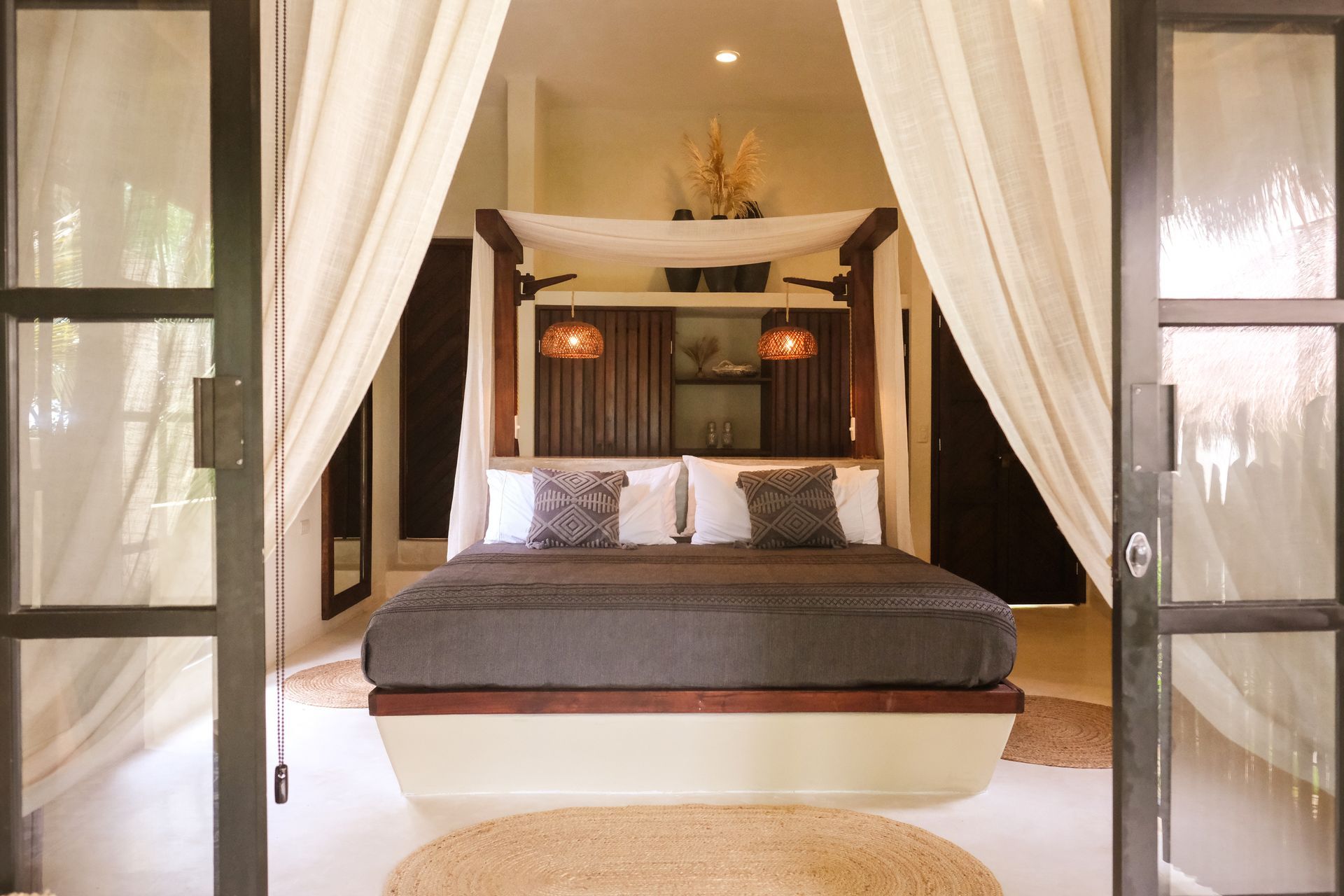 Bedroom with four-poster bed, neutral tones, sheer curtains, and open glass doors.