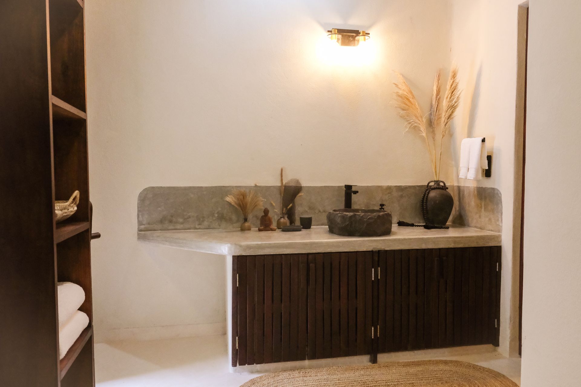 Bathroom with dark wood cabinetry, concrete countertop, stone sink, and dried plant decor.