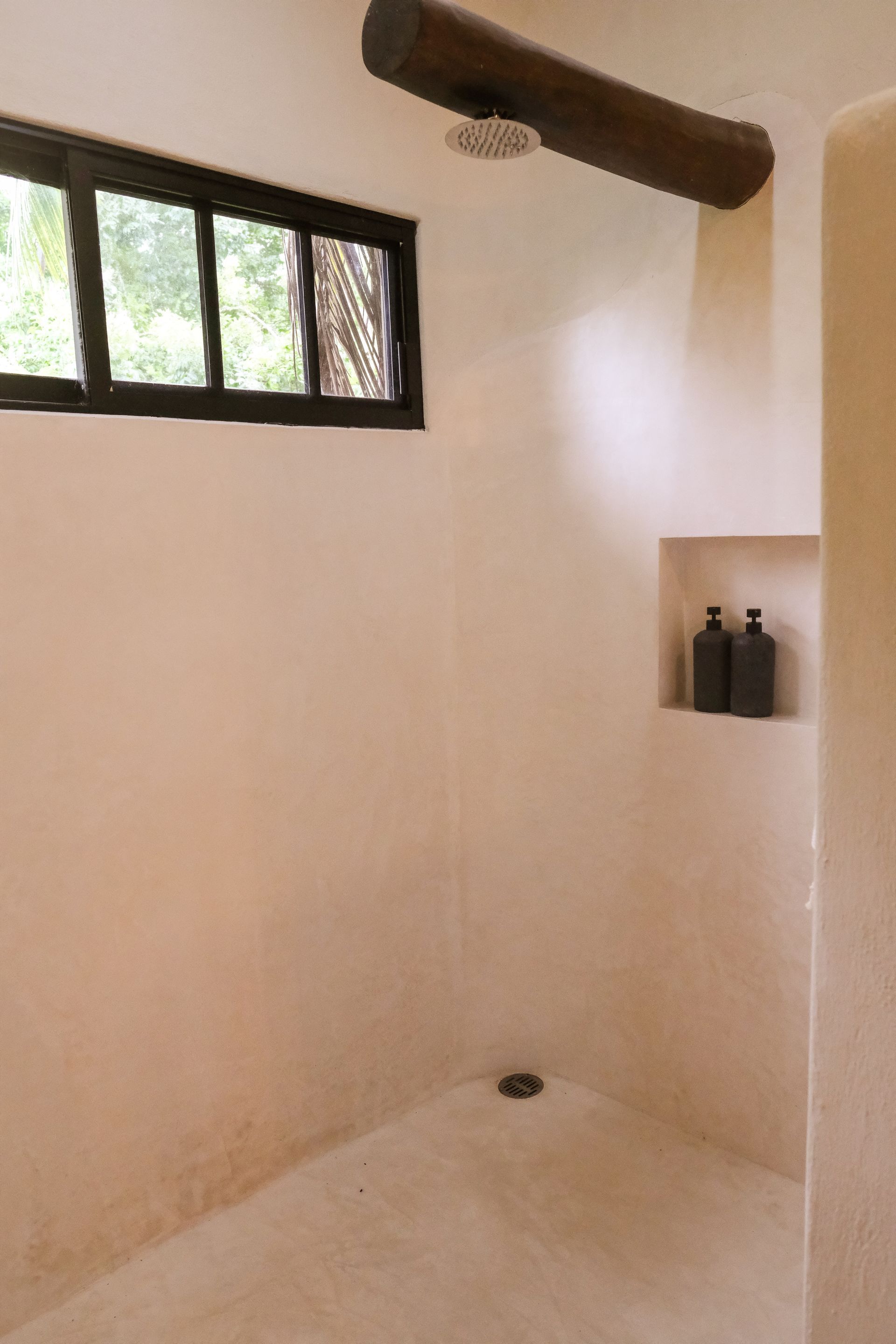 Shower with beige walls, a wood beam shower head, a small window, and built-in shelf.