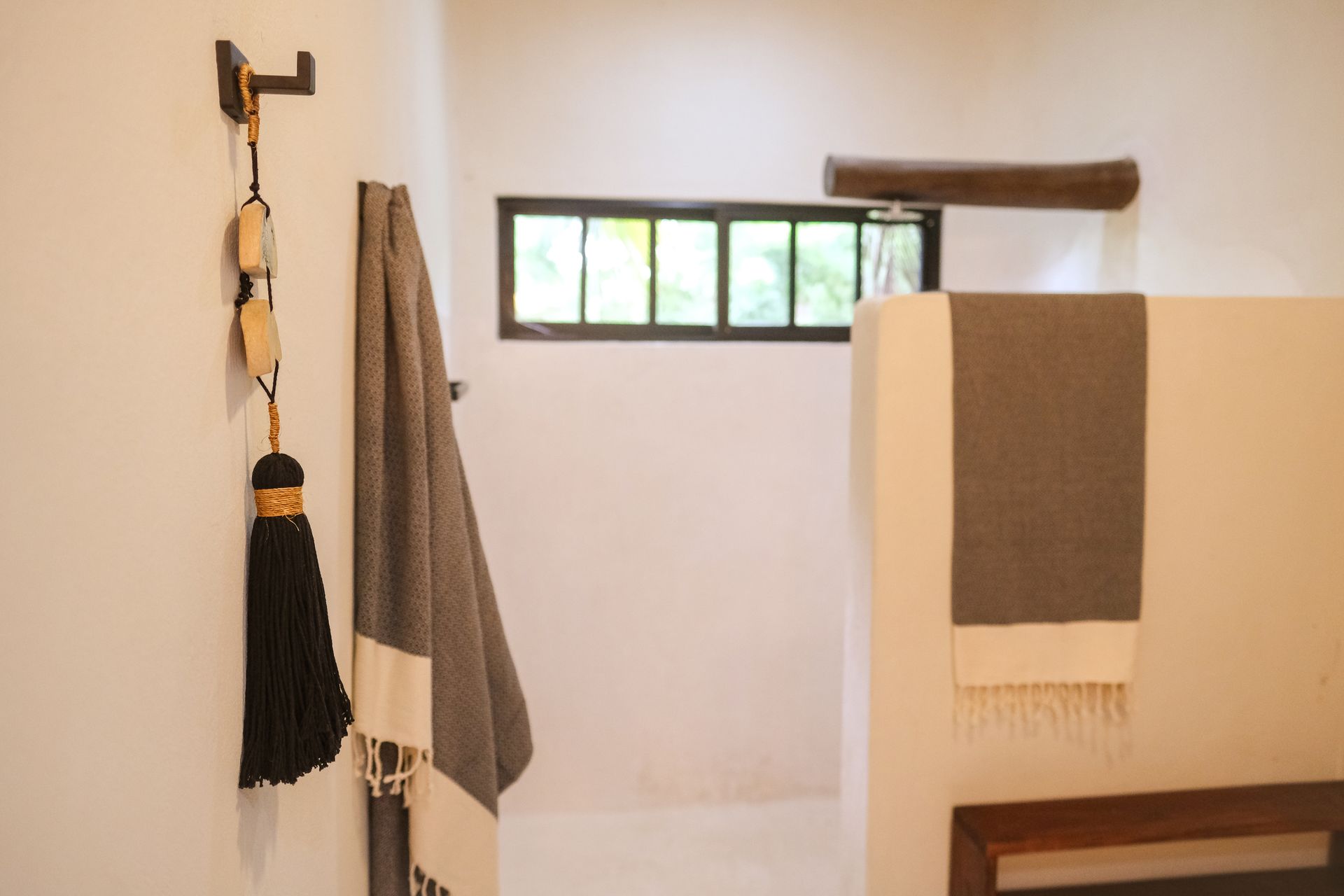 Bathroom with white walls, window, and gray towels hanging from a hook and a partition.