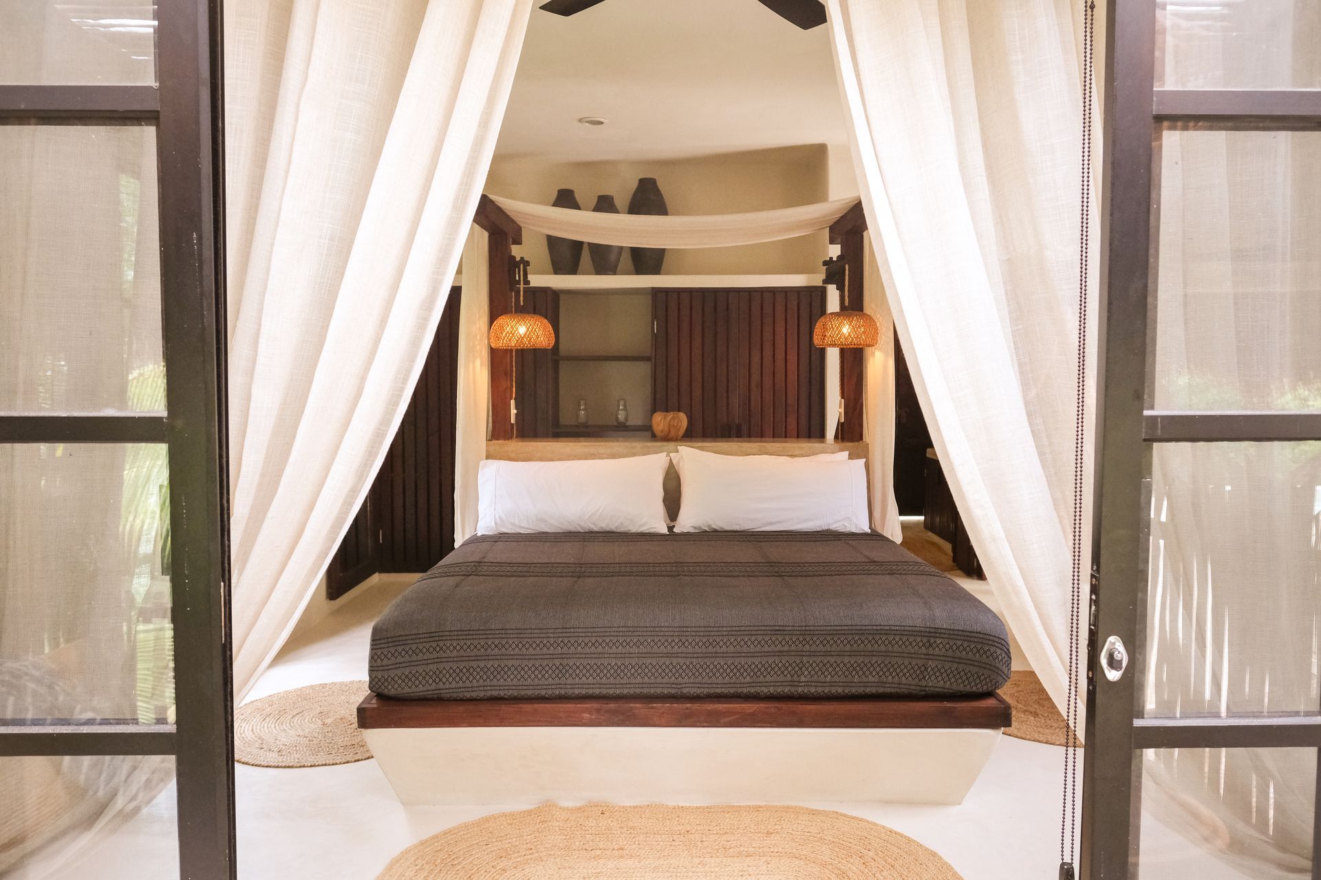 Bedroom interior with bed, draped curtains, and open glass doors.
