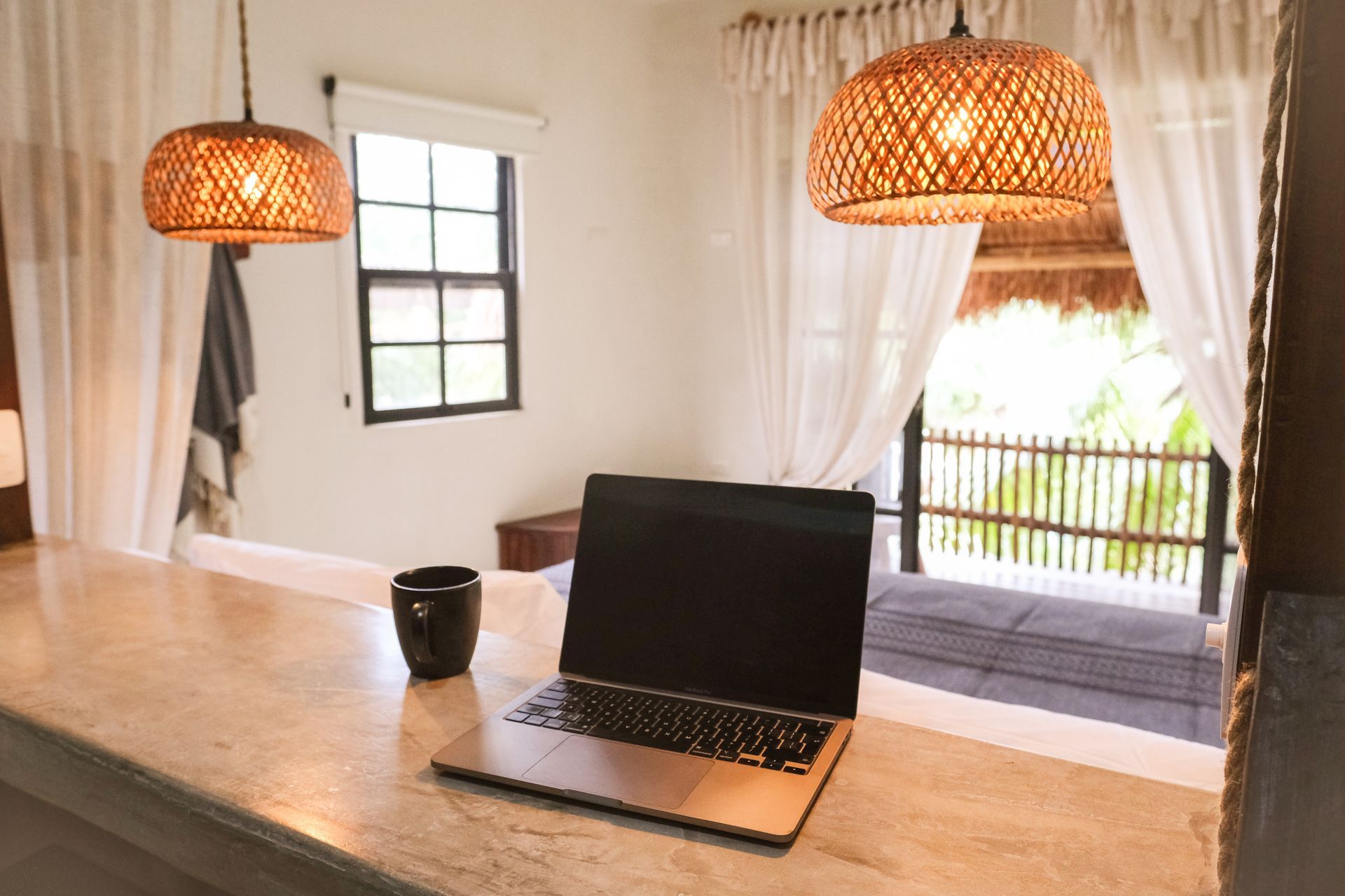 Laptop on counter with a coffee cup, wicker pendant lights, and an open doorway to a balcony.