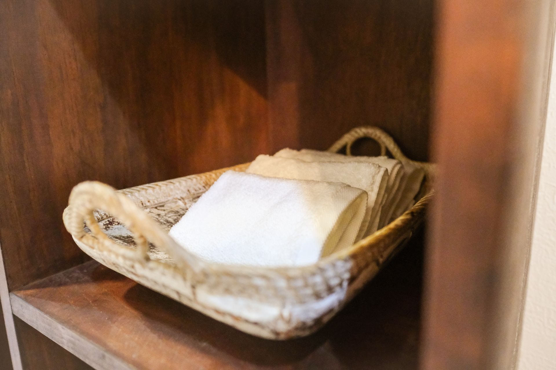 Basket of folded white cloths on a wooden shelf.