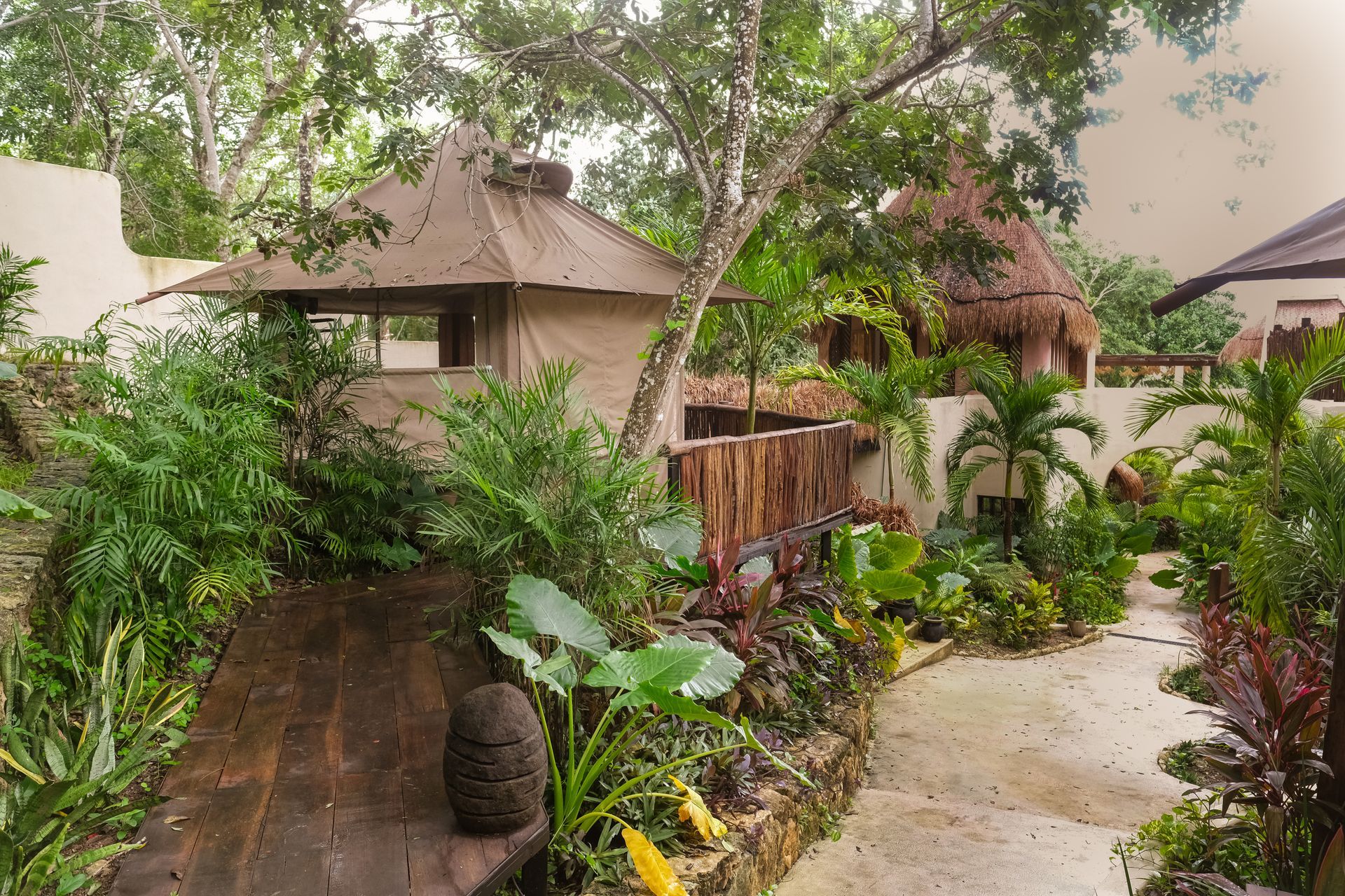 Path through lush, tropical vegetation, leading past buildings with thatched roofs and wooden accents.