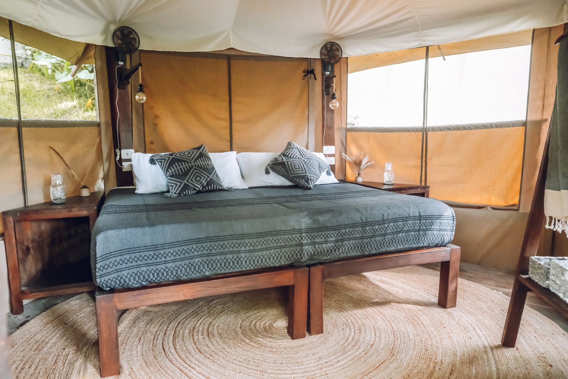 Cozy glamping tent interior with a large bed, woven rug, and natural wood furniture.