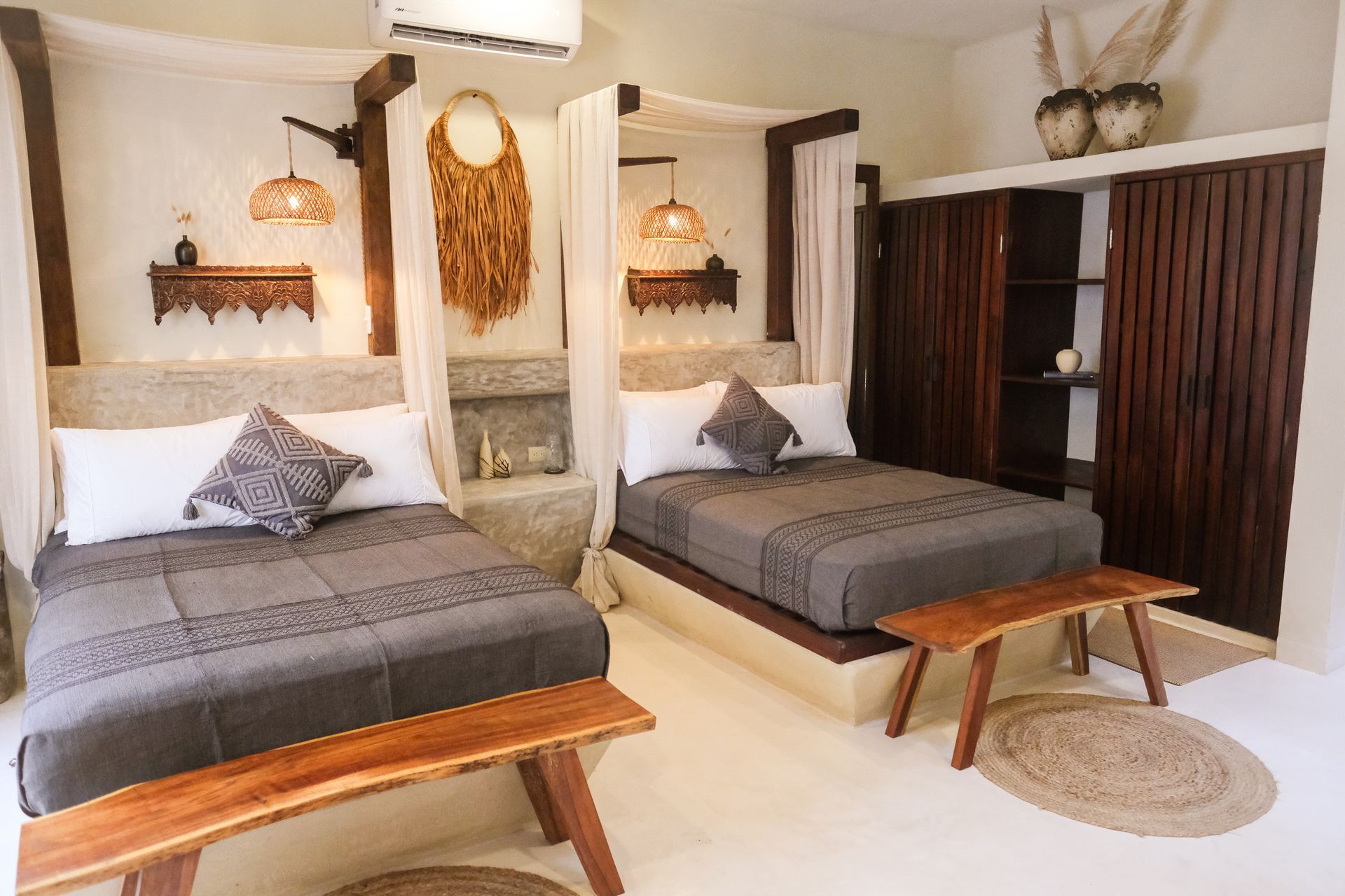 Two beds in a white-walled room with wooden accents, benches, and decorative elements.