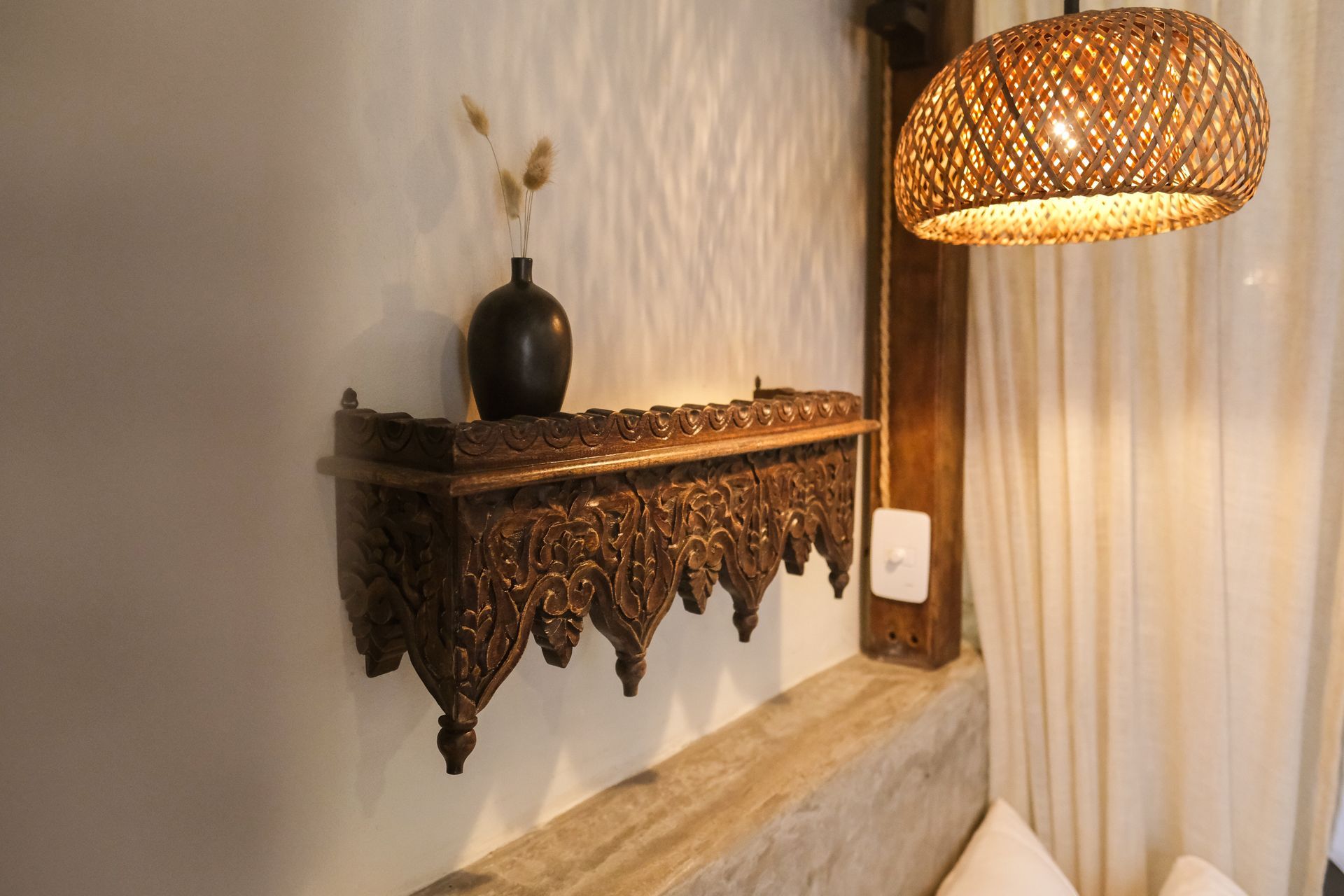 Ornate wooden shelf with vase and dried flowers; wicker pendant light.