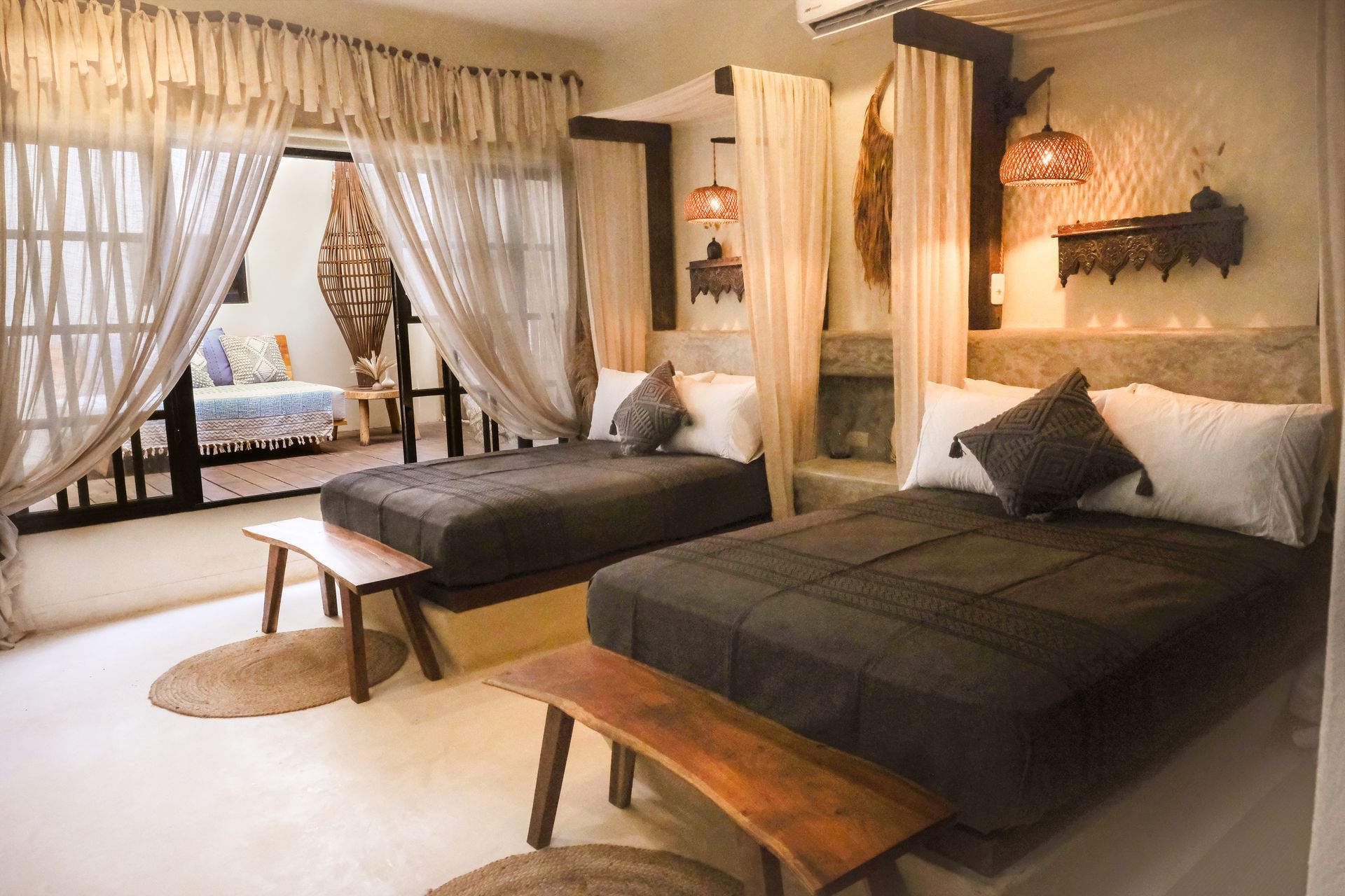 Bedroom with two beds, dark bedding, wooden benches, sheer curtains, and access to a balcony.