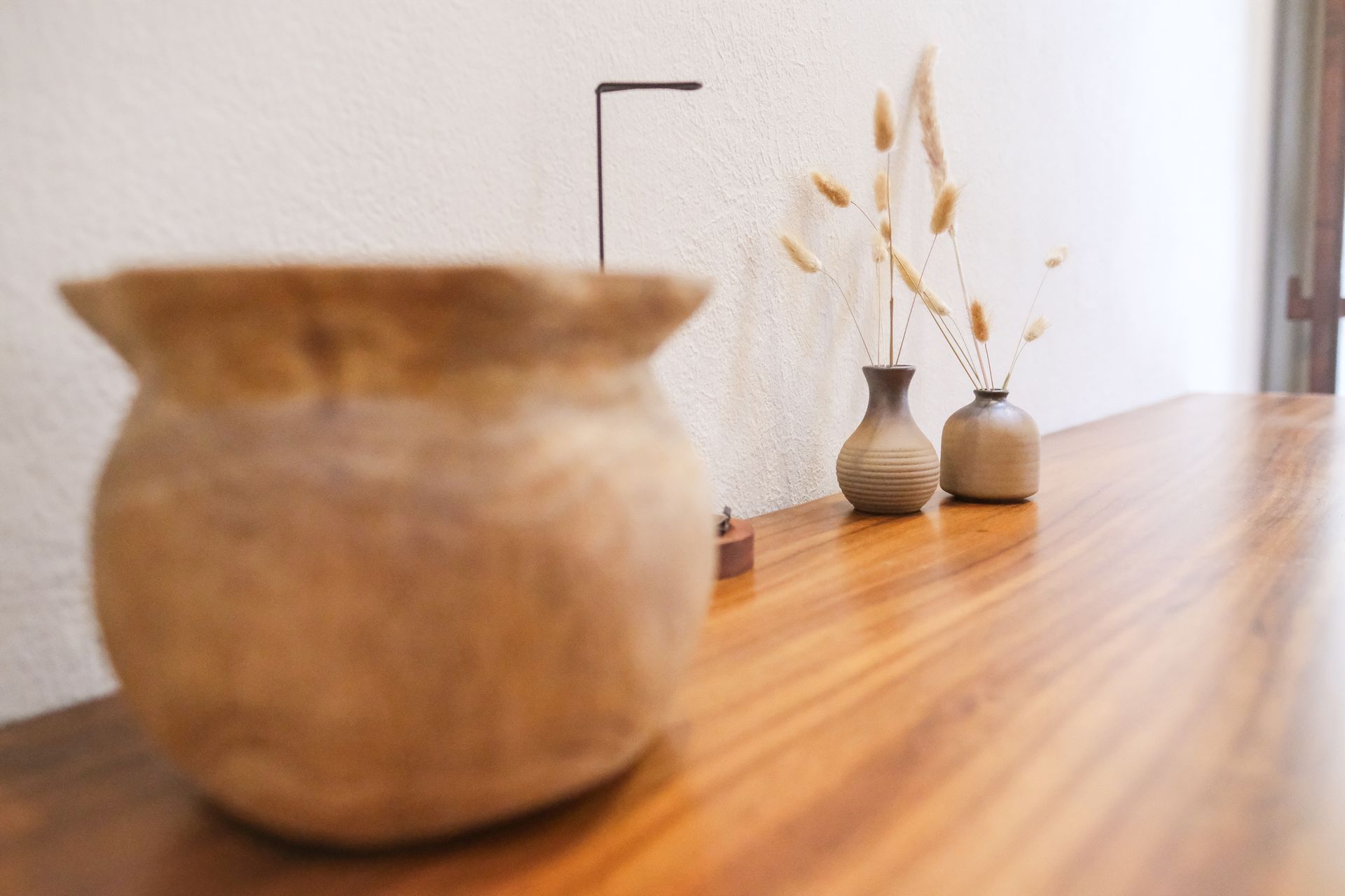 Wooden table with pottery vase in the foreground and small vases with dried plants on it.