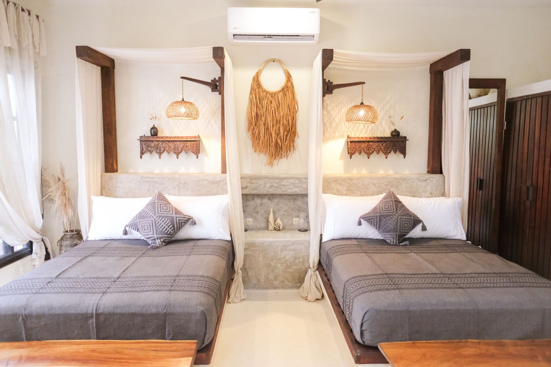 Two beds in a bohemian style room, featuring wooden frames, grey bedding, and woven wall hangings.