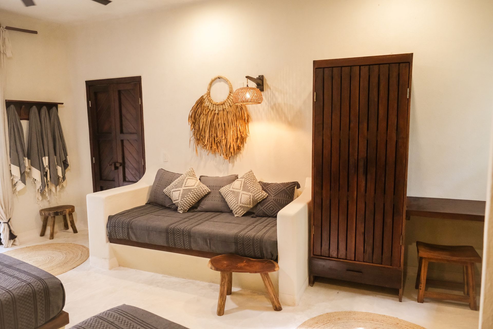 Bedroom with daybed, wooden wardrobe, stools, and wall decor; neutral tones.