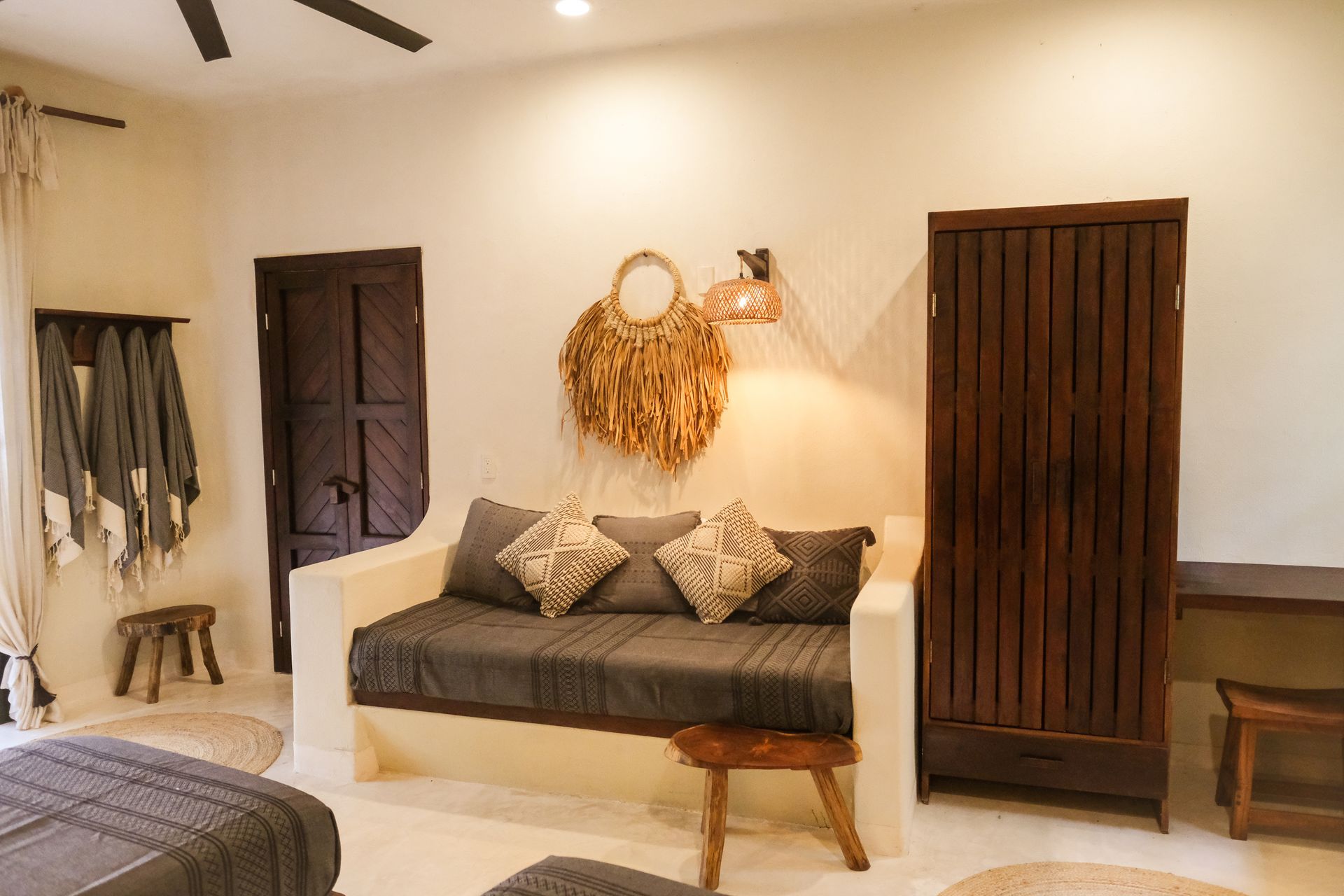 Room with daybed, dark wood armoire and door, straw decor, and small stools.