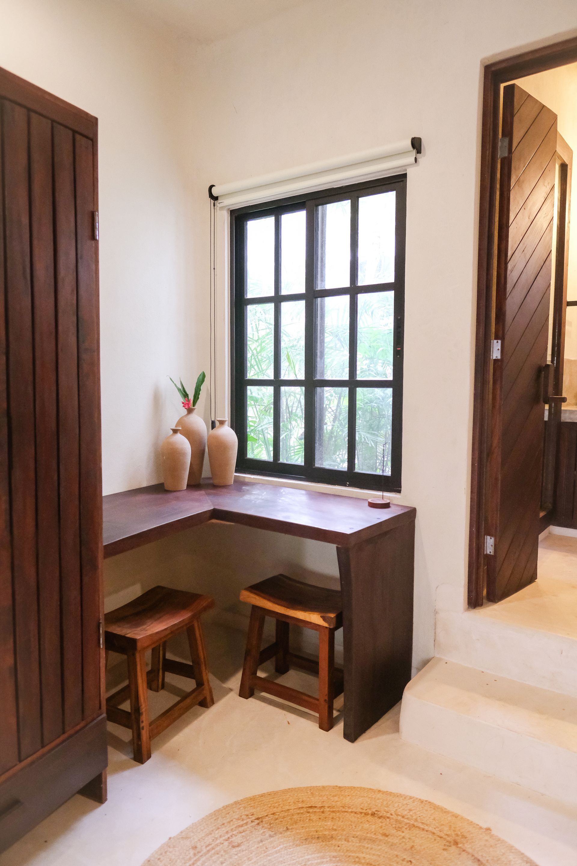 L-shaped wooden desk and stools under a window, next to a dark wooden door and cabinet.