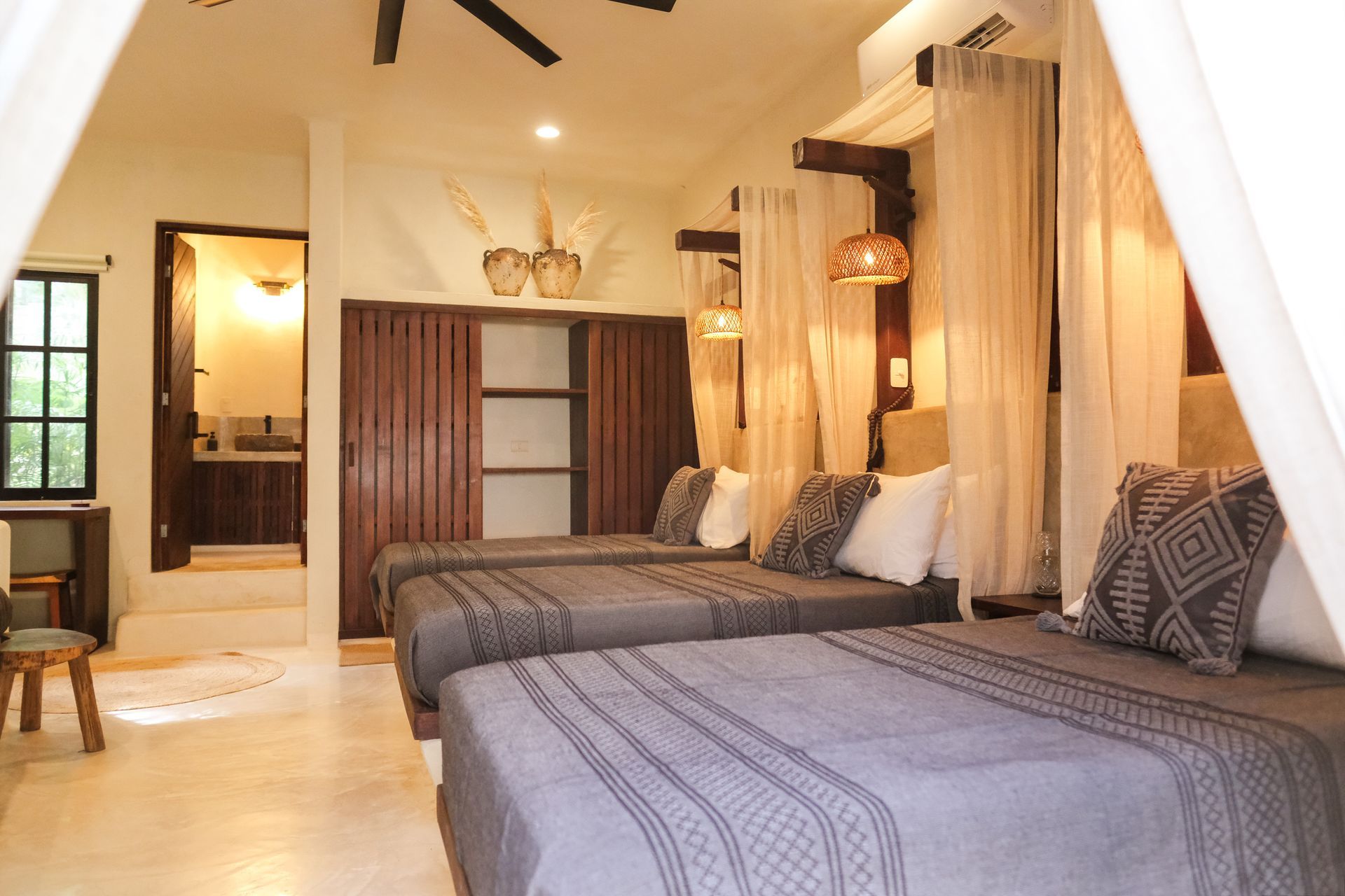 Bedroom with three beds draped with white curtains, wooden sliding doors, and a bathroom entrance.