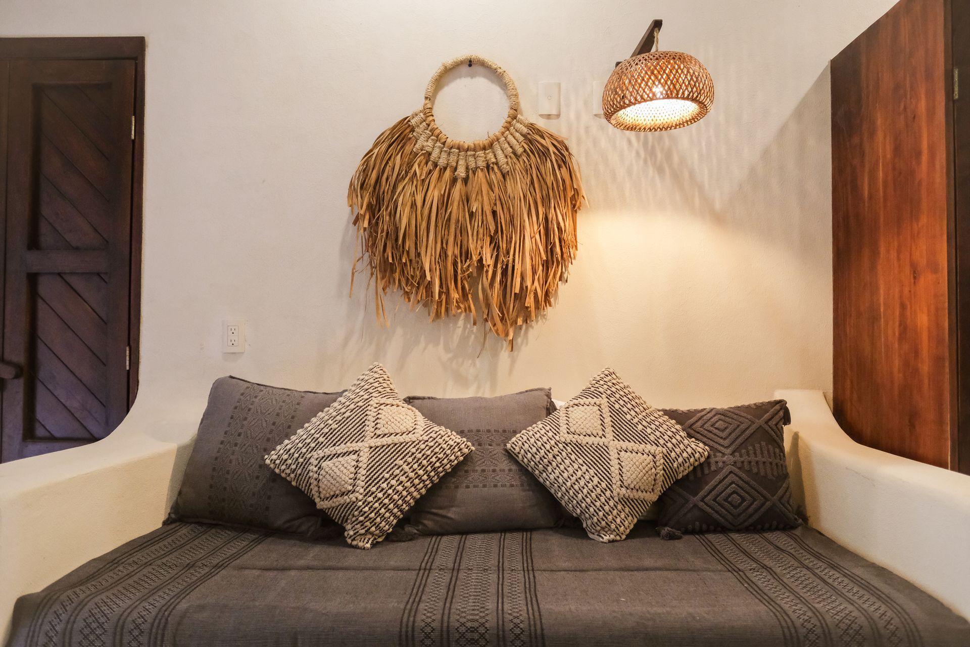 Cozy seating area with gray cushions, a woven wall hanging, and a pendant lamp against a white wall.