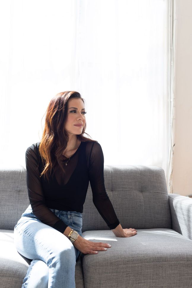 A woman in a black shirt is sitting on a couch and smiling.