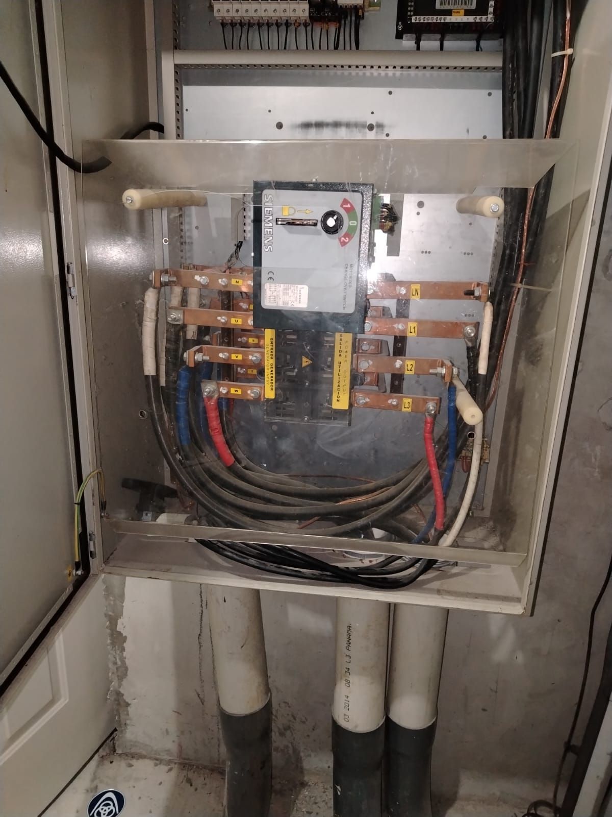 Panel eléctrico con cables e interruptores, protegido por una cubierta transparente. Los cables son negros, rojos y azules.