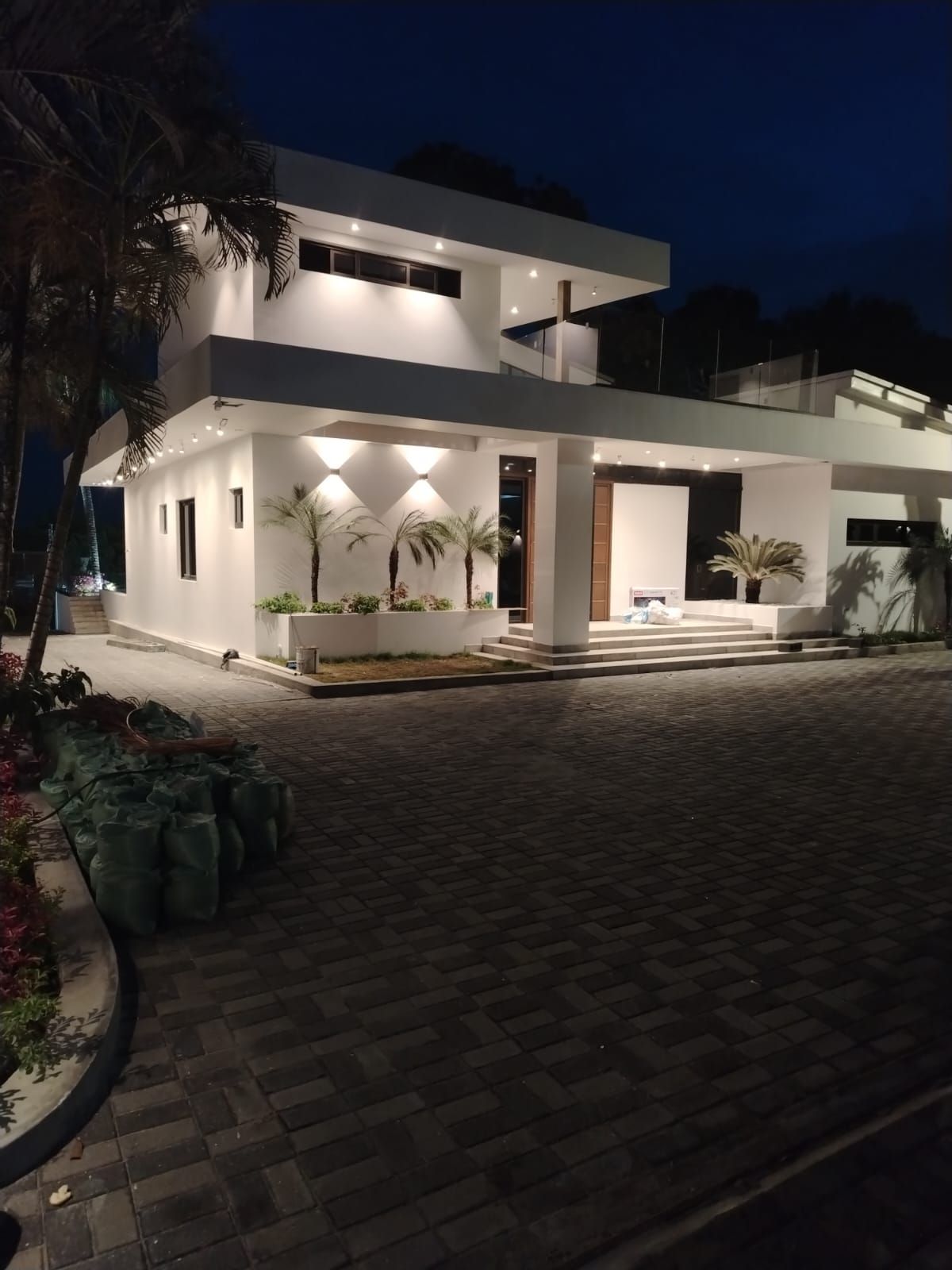 Moderna casa blanca de dos plantas con exterior iluminado, escalones que conducen a la entrada y cielo nocturno oscuro.