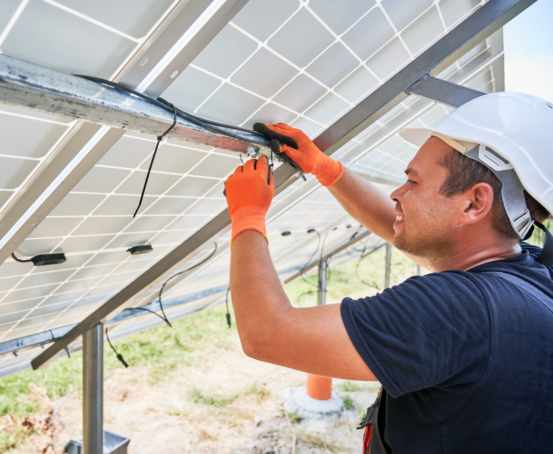 Instalador de paneles solares con guantes naranjas y casco, cableando paneles.