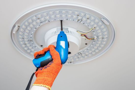 Electricista con herramientas y guantes sosteniendo cable eléctrico blanco.