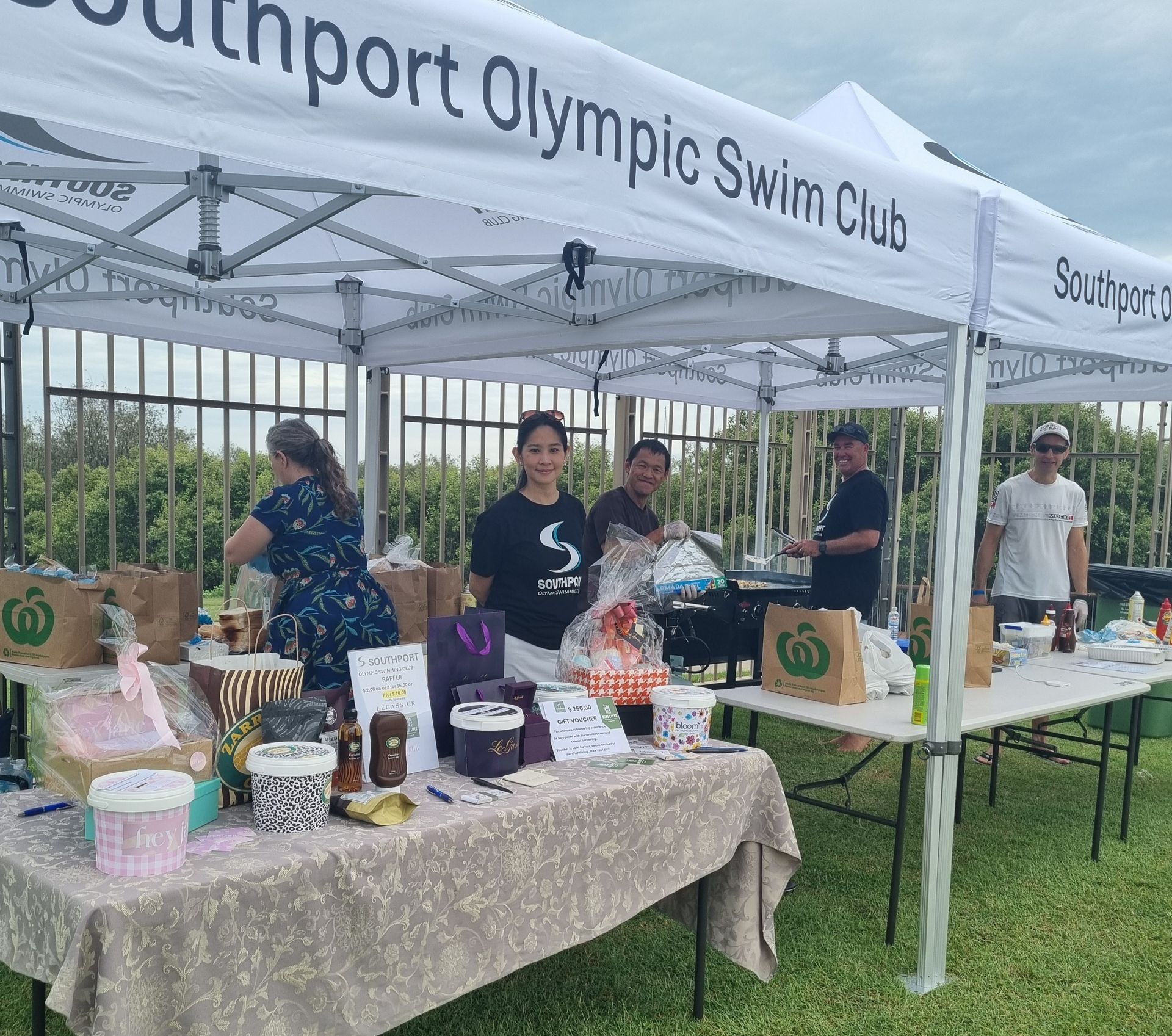 People at a Southport Olympic Swim Club stall selling goods at an outdoor event.