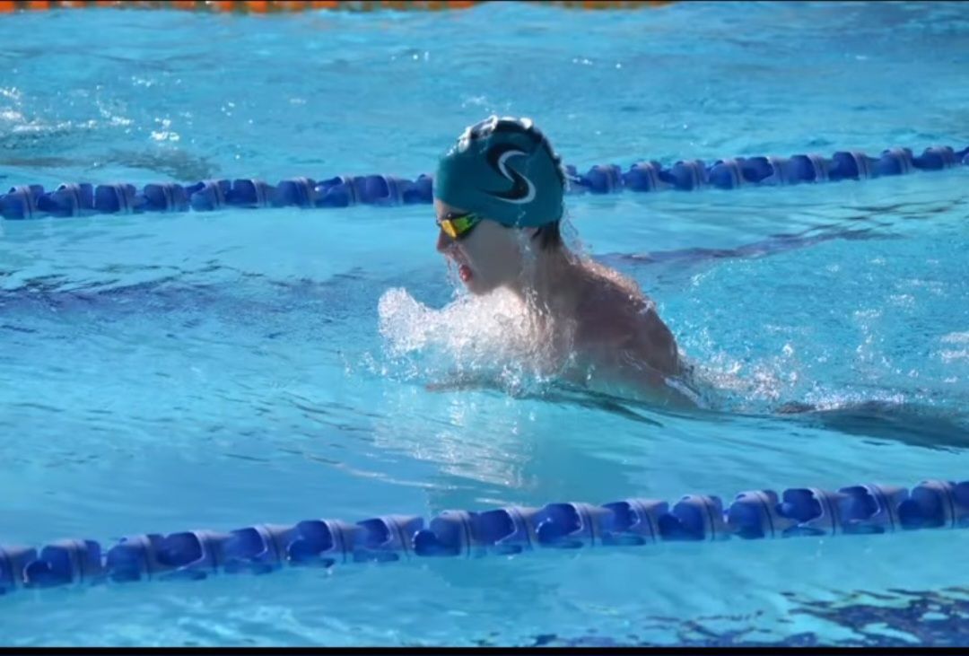 Swimmer in teal cap and goggles doing the breaststroke in a blue pool.