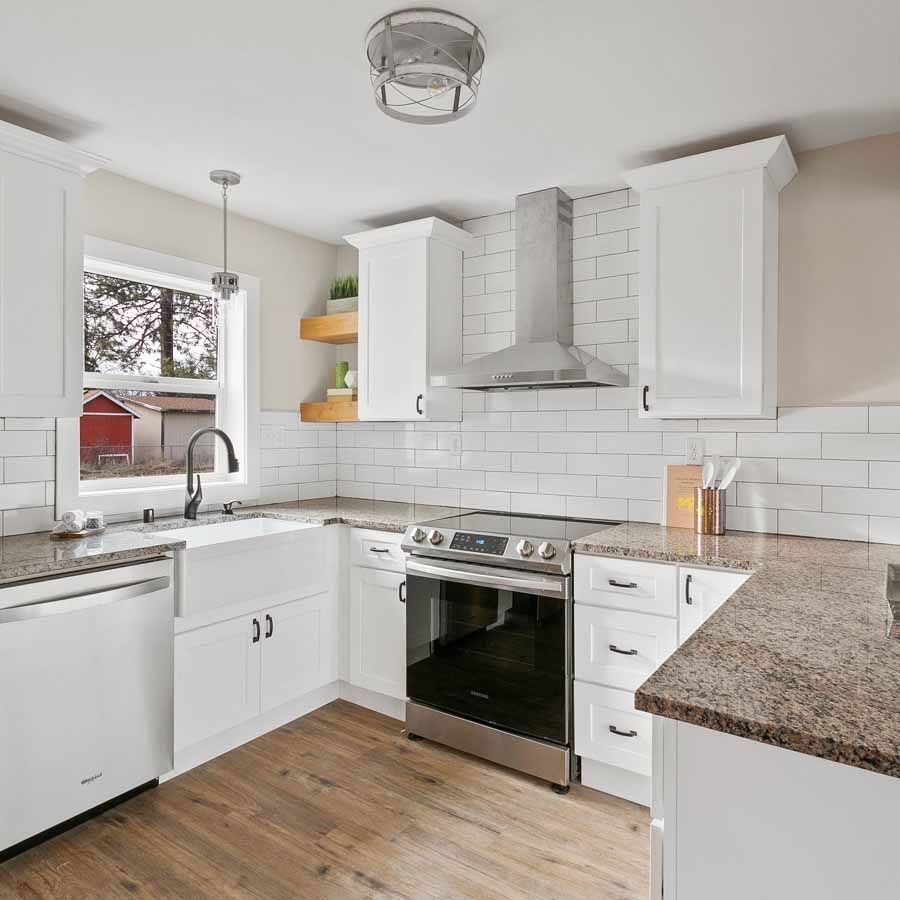 A kitchen with white cabinets , a stove , a sink , and a window.