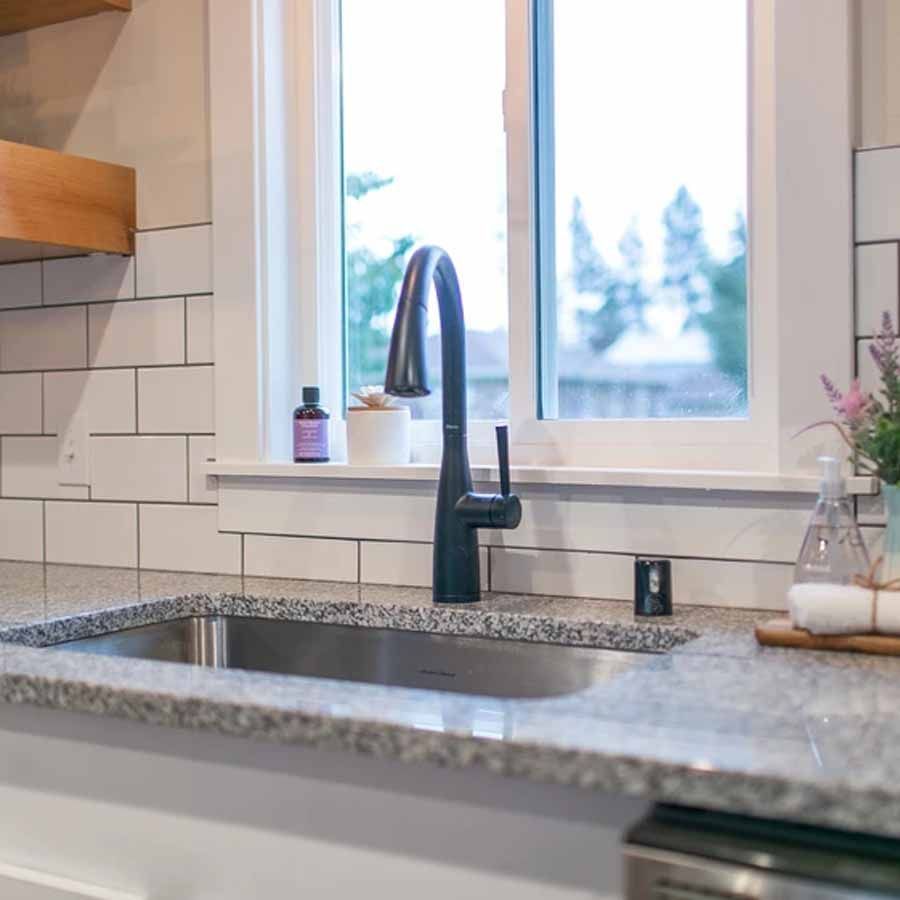 A kitchen sink with a faucet and a window in the background.