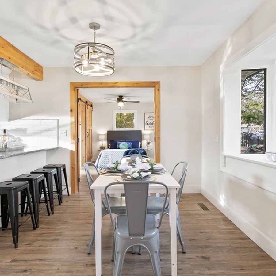 A dining room with a table and chairs and a bedroom in the background.