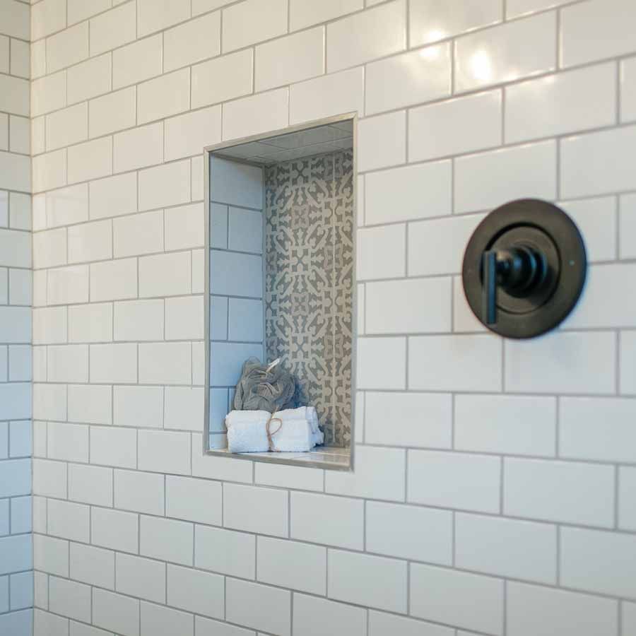 A shower with white tiles and a black shower head.