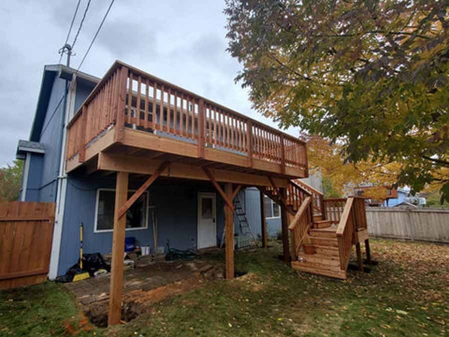 A blue house with a wooden deck and stairs in the backyard.