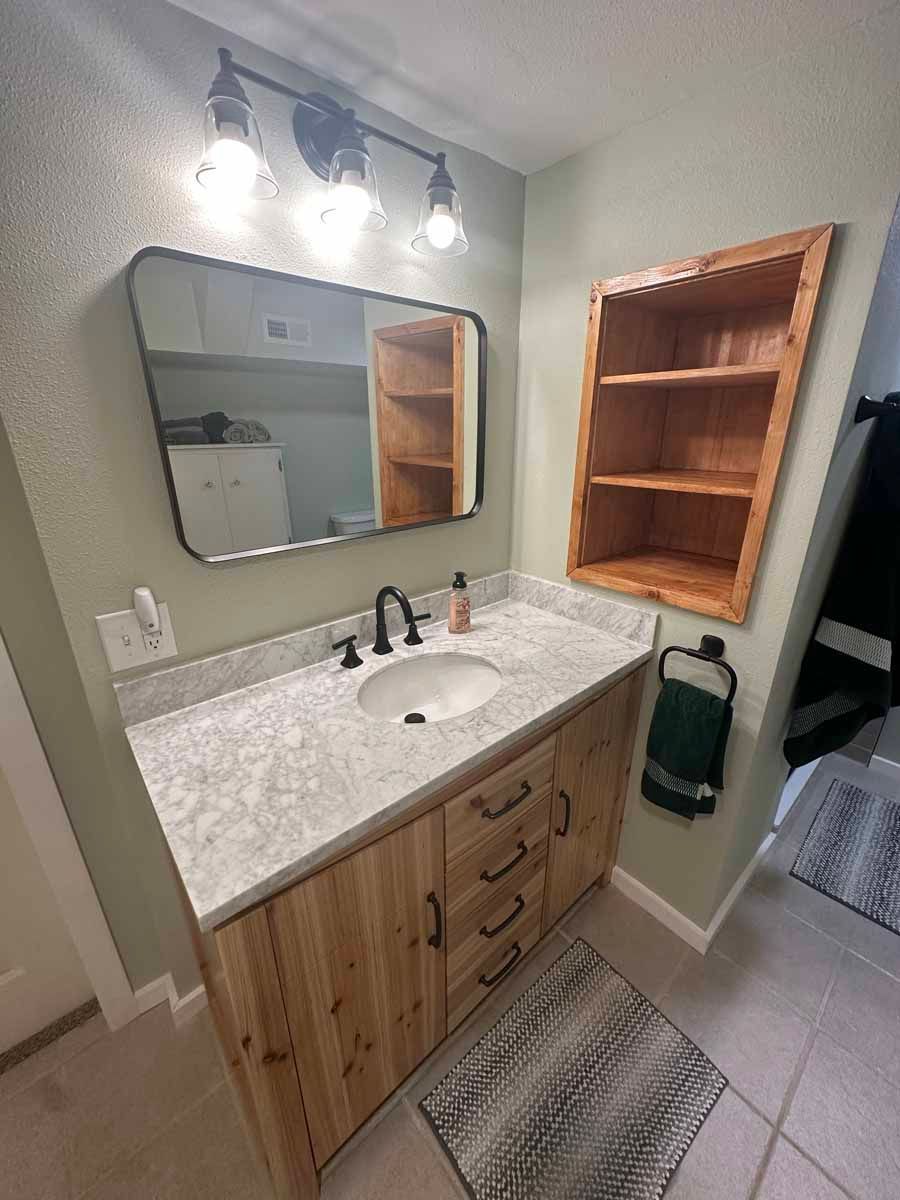 A bathroom with a sink , mirror and shelves.