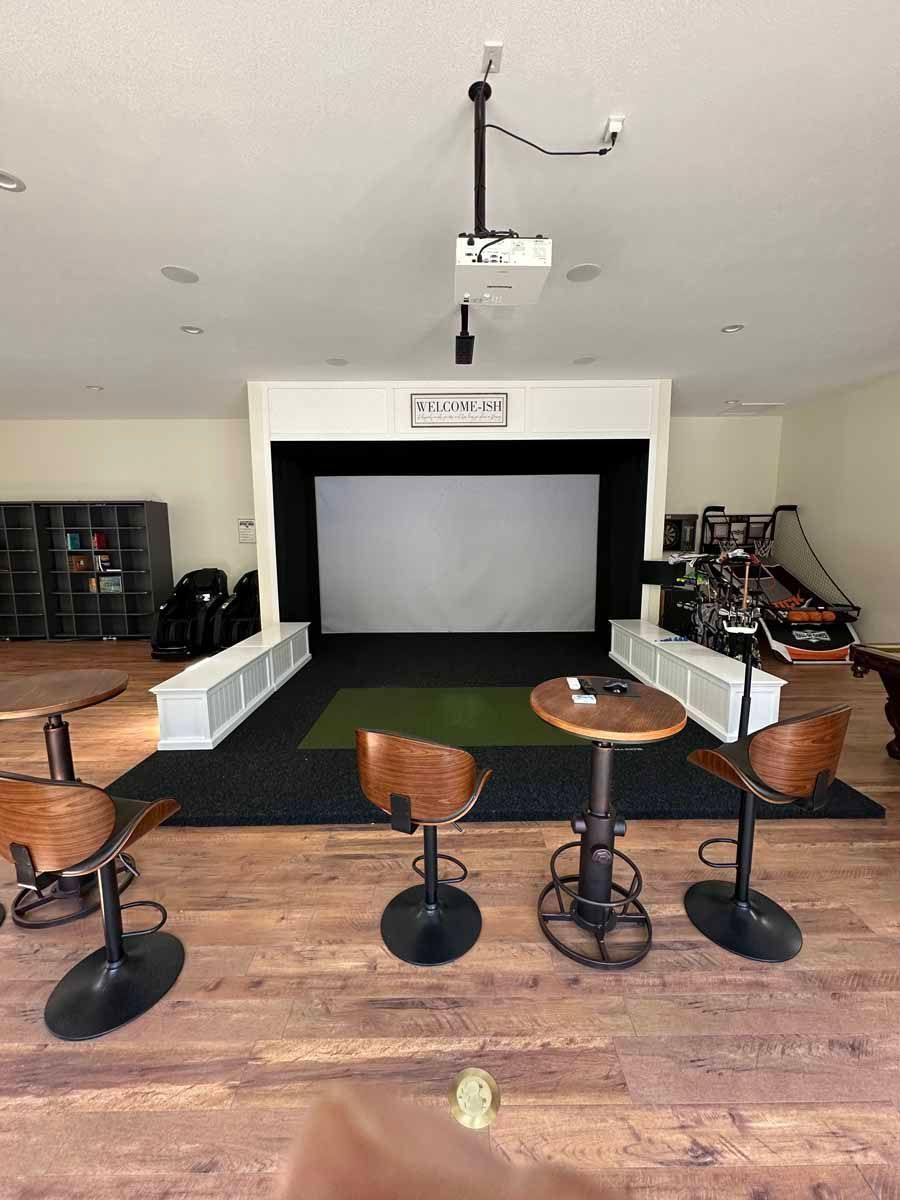 A room with three tables and chairs in front of a large screen.