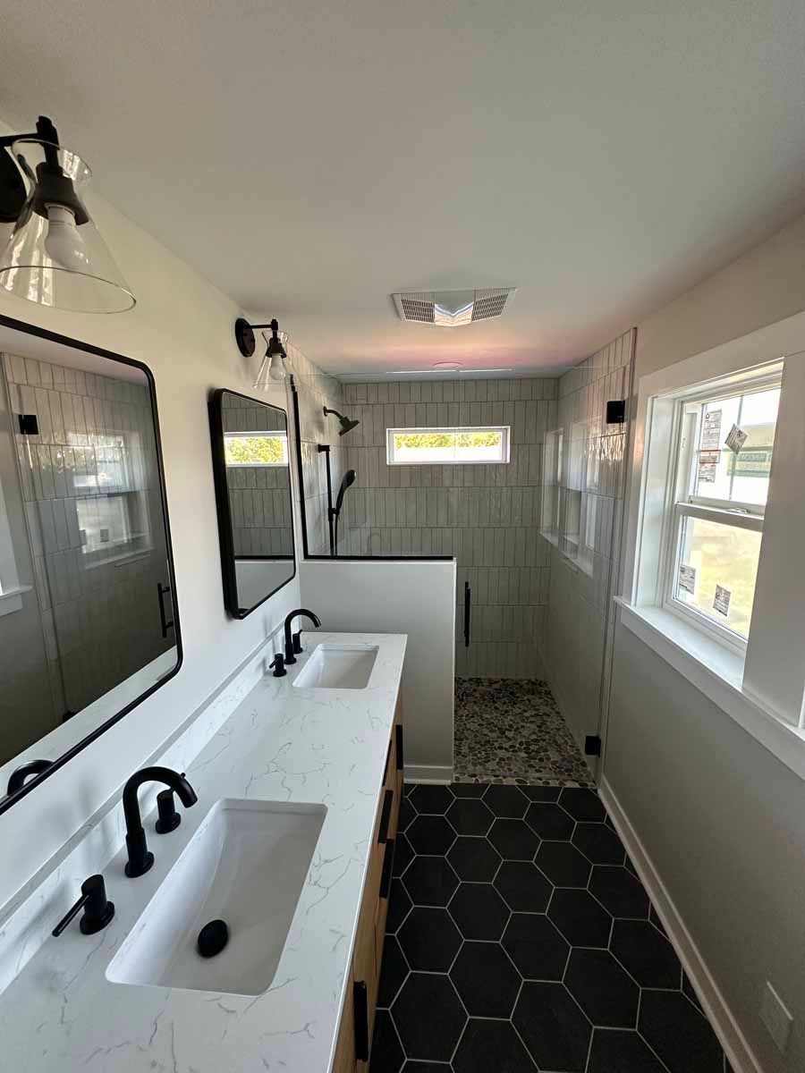 A bathroom with two sinks , two mirrors , and a walk in shower.