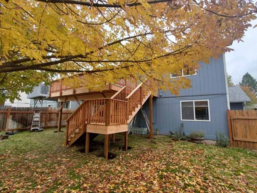 A blue house with a wooden deck and stairs in the backyard.