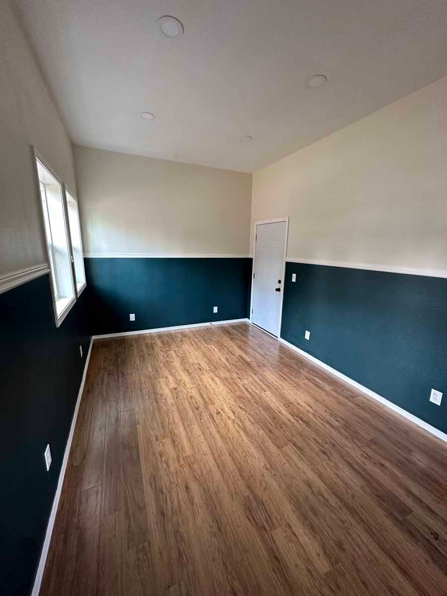 A large empty room with hardwood floors and green and white walls.