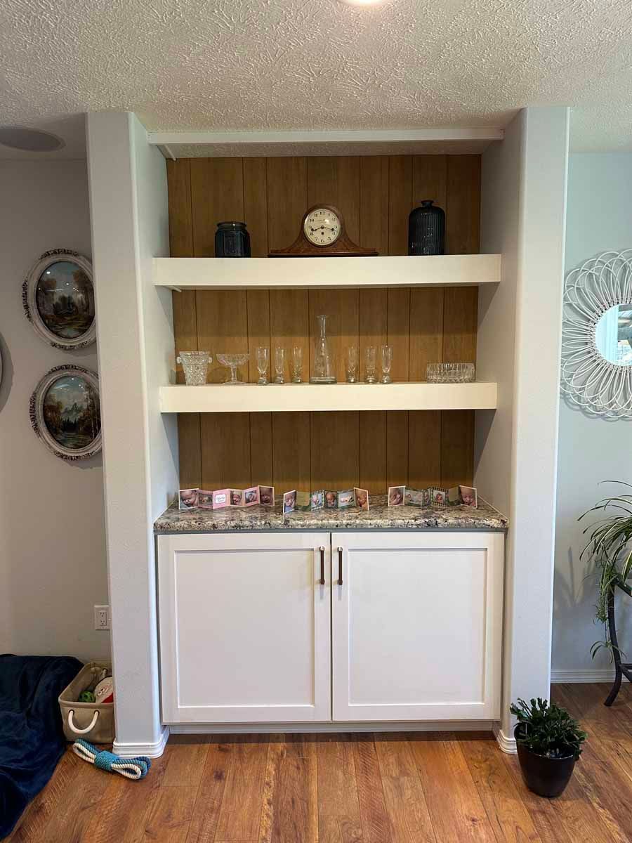 A living room with hardwood floors and a shelf with glasses on it.