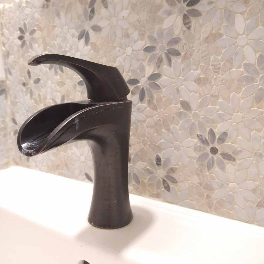 A bathroom sink with a black faucet and flowers on the wall