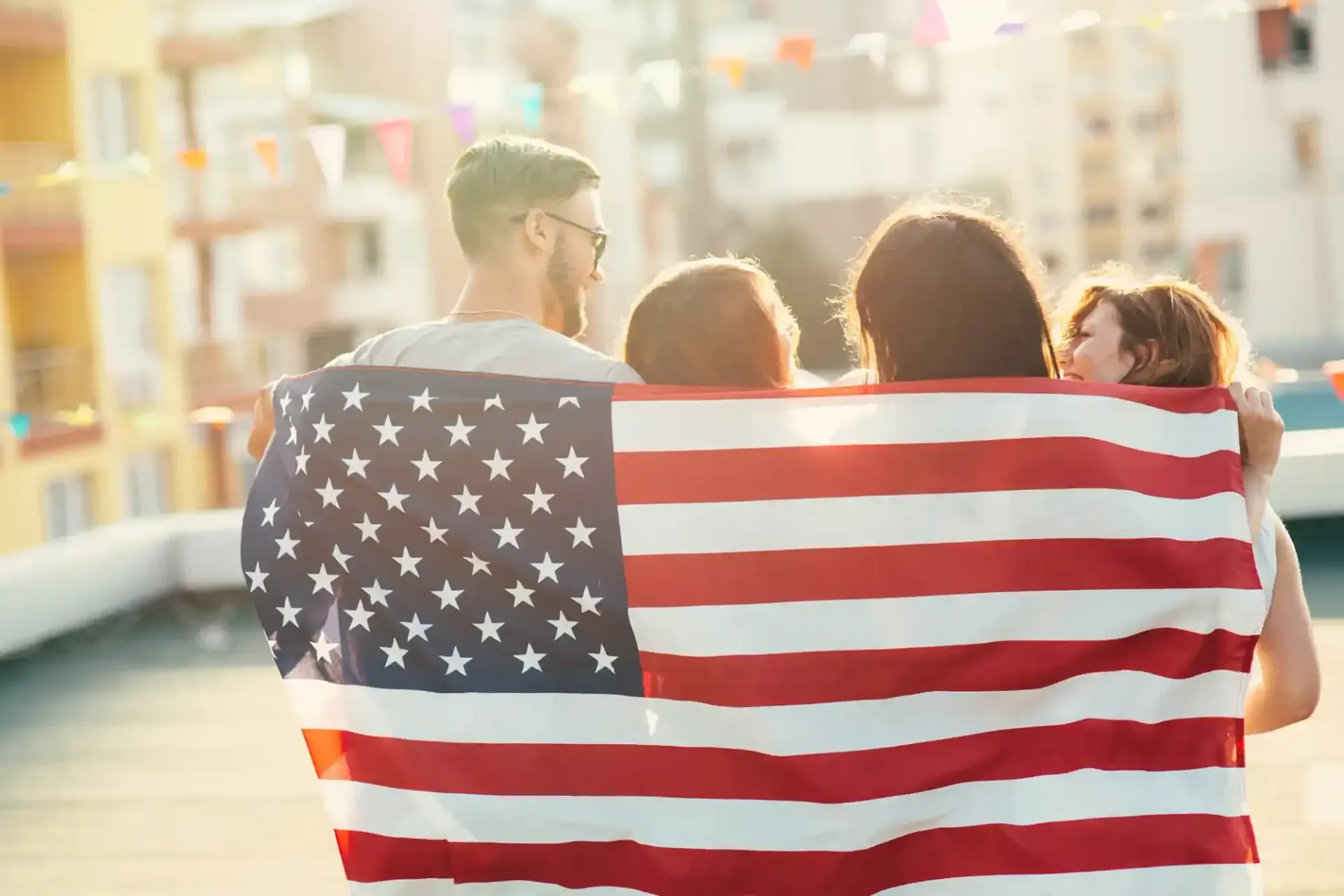 People holding up an American flag on a rooftop with colorful flags in the background.
