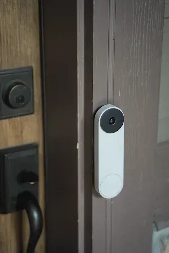 White doorbell camera on a brown door, near a black doorknob and lock.