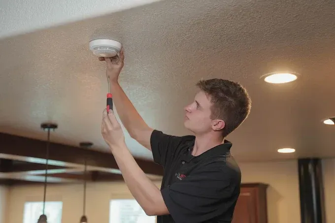 Man installing a smoke detector on a ceiling in a home, using a screwdriver.