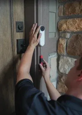 White doorbell camera on a brown door, near a black doorknob and lock.