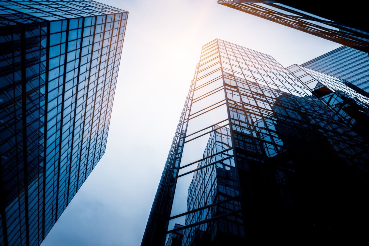 Skyscrapers with glass facades, angled upward towards the bright sky.