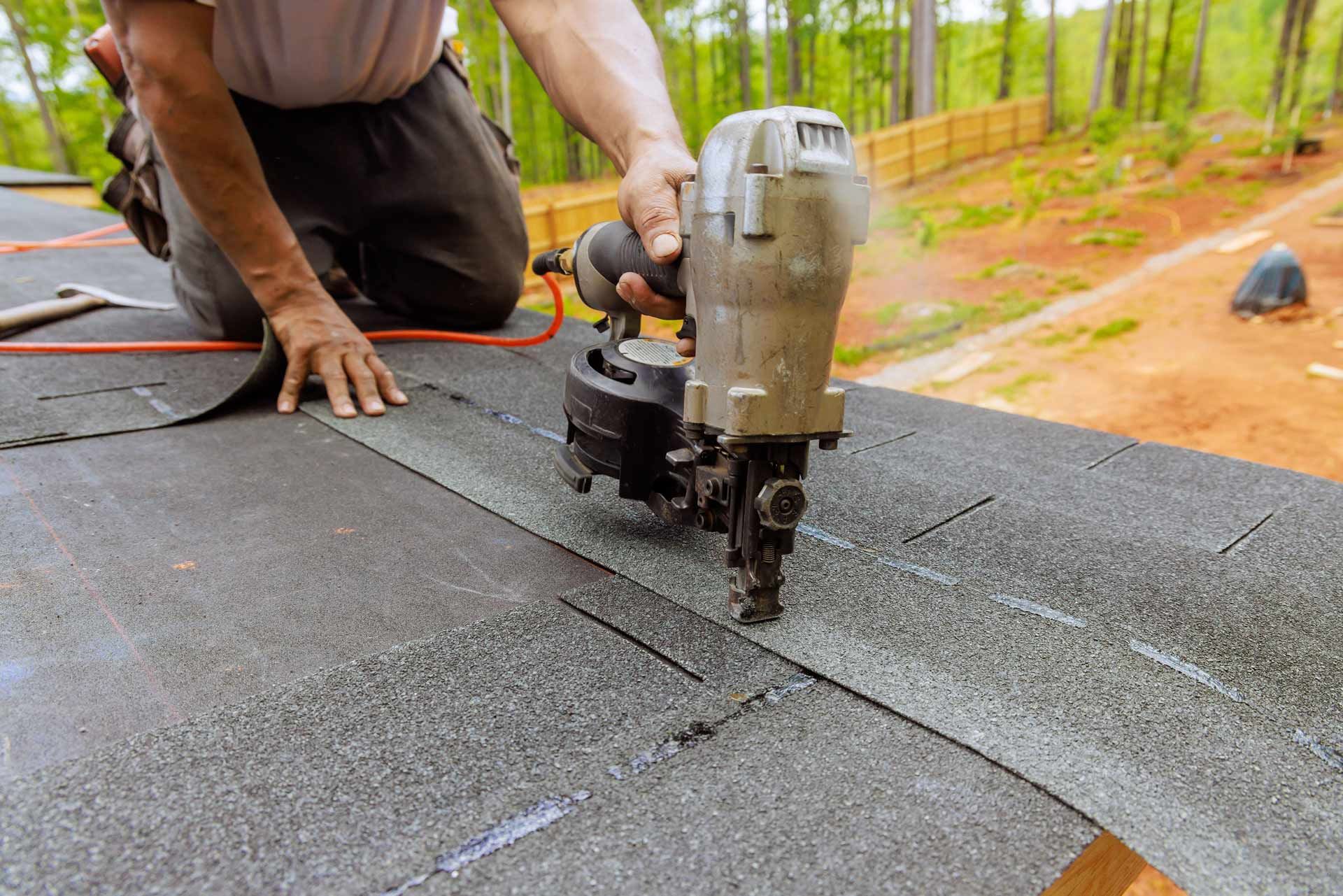 Roofer uses a nail gun to install asphalt shingles on a roof