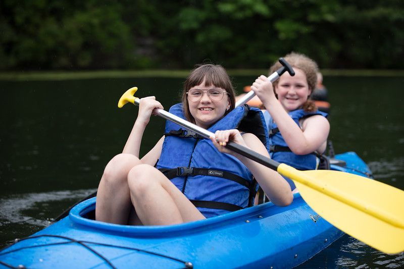 two girls are paddling a blue kayak on a lake .