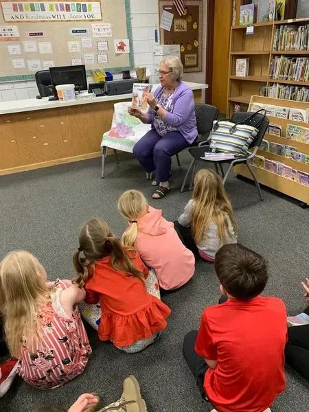 Children seated on a library carpet listening to a speaker in a bright room with bookshelves. Children seated on a library carpet listening to a speaker in a bright room with bookshelves.